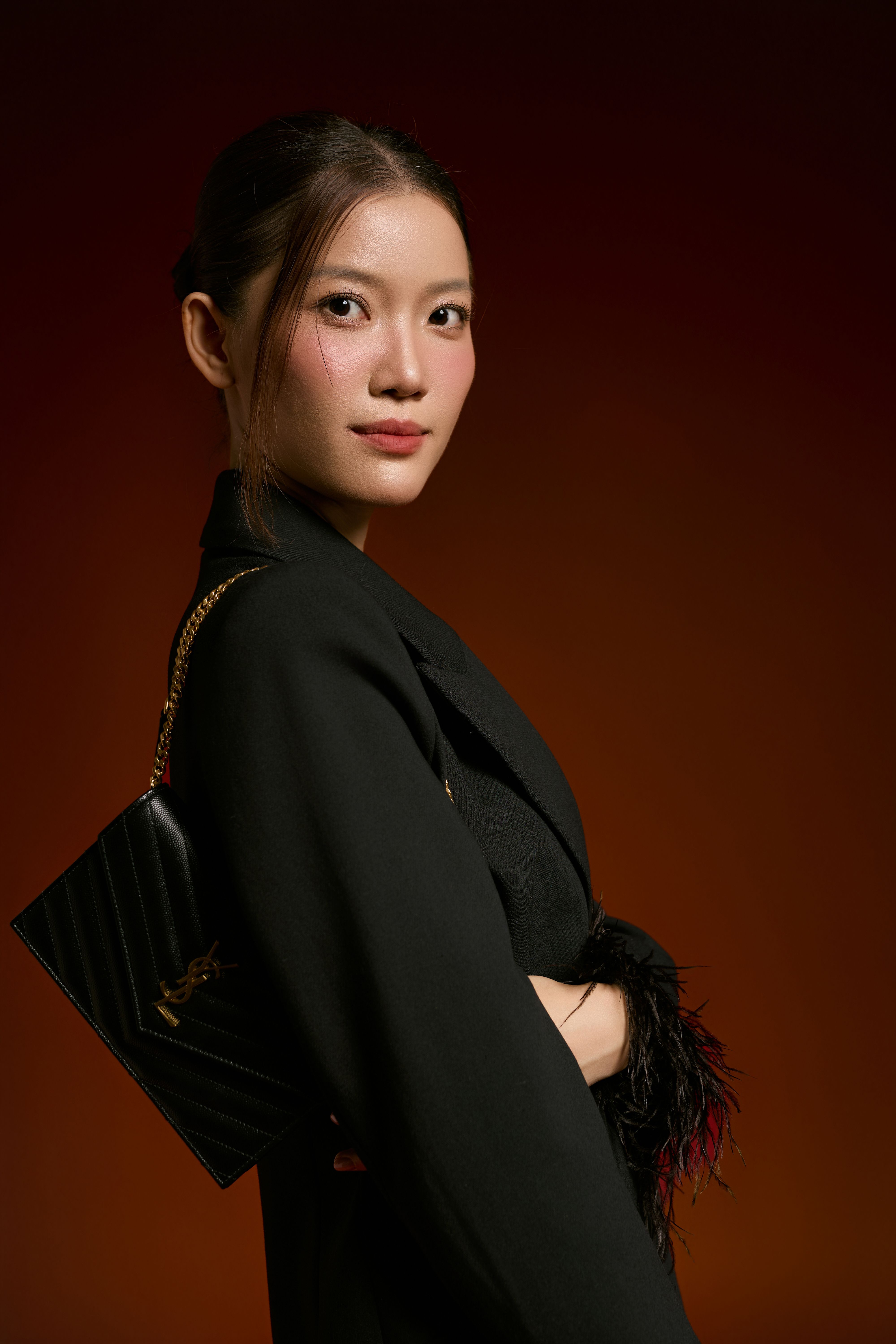 Stylish young woman in a black outfit poses with a designer handbag against a warm background.