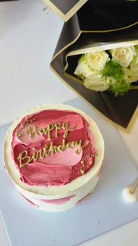 Top view of a stylish birthday cake with pink frosting and white roses nearby.