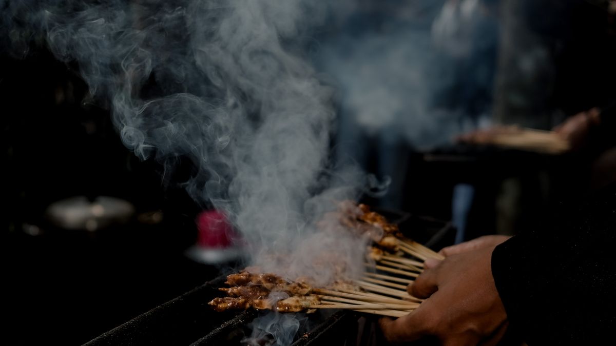 Delicious satay skewers being grilled and smoked in a vibrant street market in West Java, Indonesia.