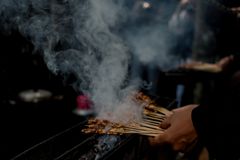 Delicious satay skewers being grilled and smoked in a vibrant street market in West Java, Indonesia.