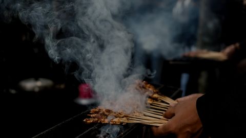 Delicious satay skewers being grilled and smoked in a vibrant street market in West Java, Indonesia.