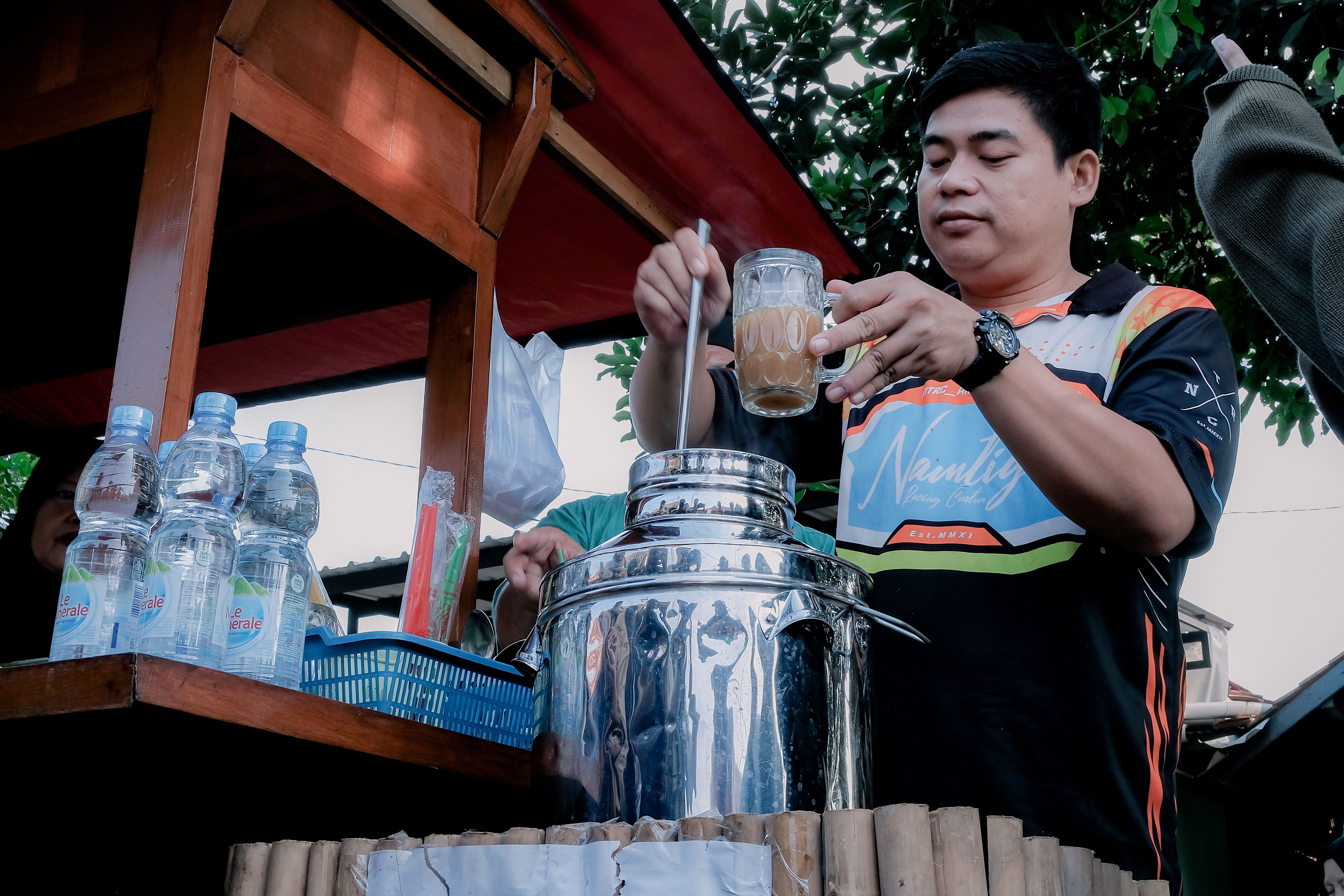 Man at West Java street stall making a traditional Indonesian beverage outdoors.