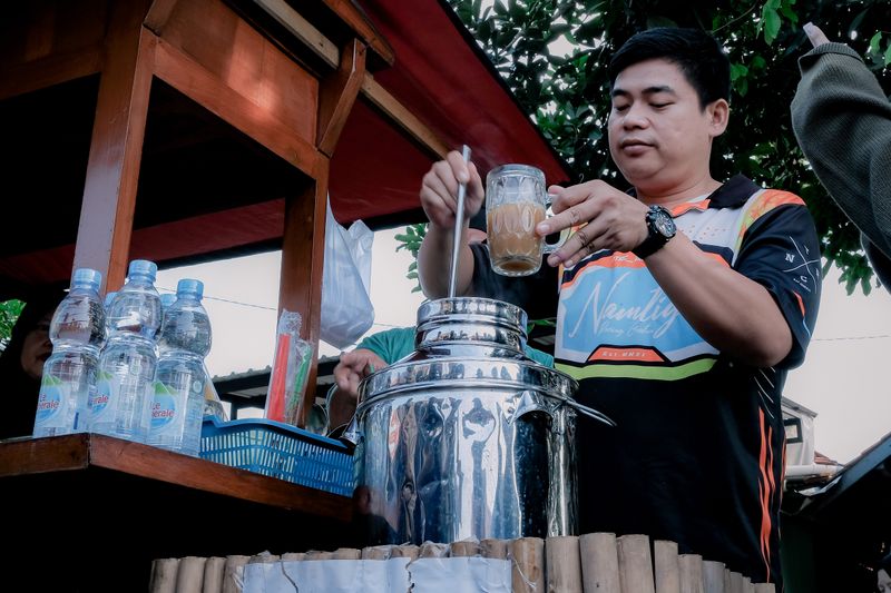 Man at West Java street stall making a traditional Indonesian beverage outdoors.