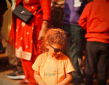 A young child in sunglasses enjoys a vibrant color festival in Nepal, celebrating tradition.