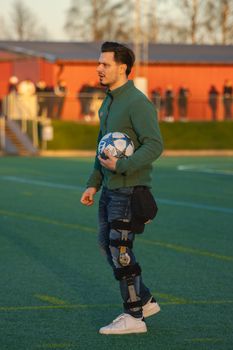 A man with a knee brace holding a soccer ball on a sports field during the day.
