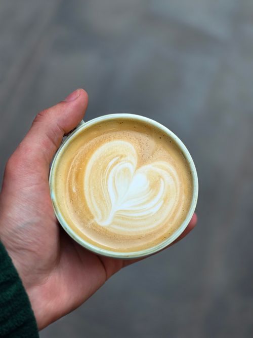 Free A cup of coffee with heart-shaped latte art, held in a hand, perfect for café and coffee lovers. Stock Photo