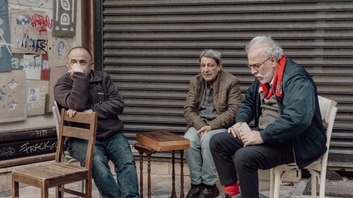Free Three older men sitting in front of a shuttered shop in Istanbul, engaged in casual conversation. Stock Photo