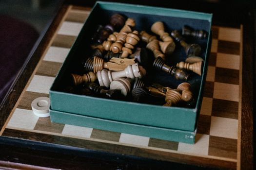 A collection of wooden chess pieces inside a green box on a chessboard.