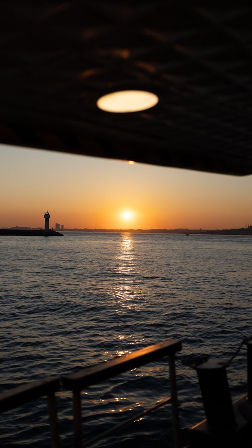 Free View of a breathtaking sunset over the Bosphorus Strait in Istanbul, featuring a silhouetted lighthouse and shimmering water. Stock Photo