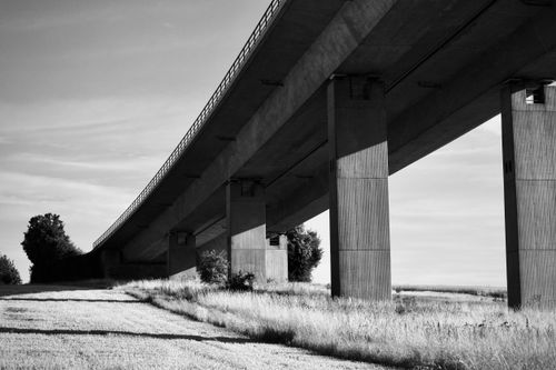 Free Artistic black and white photo of a bridge underpass highlighting architectural lines and natural contrast. Stock Photo