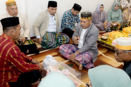 A group of adults in traditional attire participating in a cultural ceremony indoors.