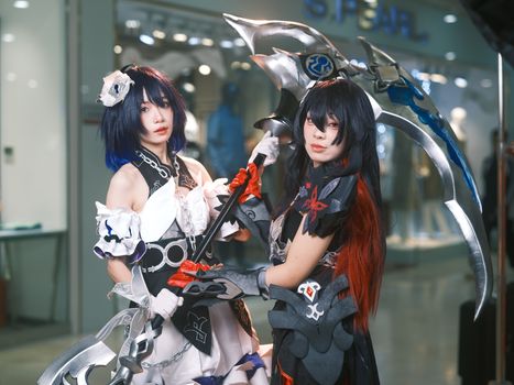 Two cosplayers striking a pose with elaborate costumes and weapons in an indoor setting.