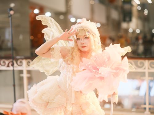 Free Captivating fairy cosplay with elaborate wings and a pink flower prop, indoors with soft lighting. Stock Photo
