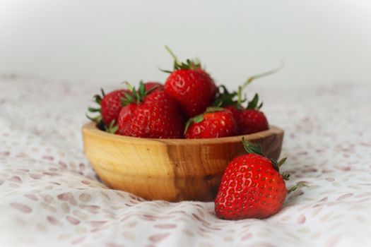 A wooden bowl filled with fresh strawberries on a soft, patterned fabric background. Perfect for healthy lifestyle and food imagery.