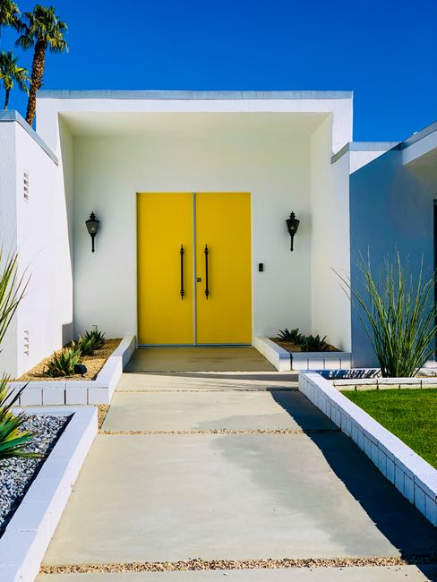 Front view of a modern house with a vibrant yellow door in Palm Springs, CA.