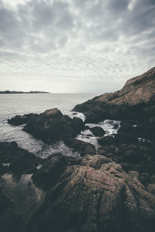 Free A moody, dramatic rocky shoreline scene with waves crashing under a cloudy sky. Stock Photo