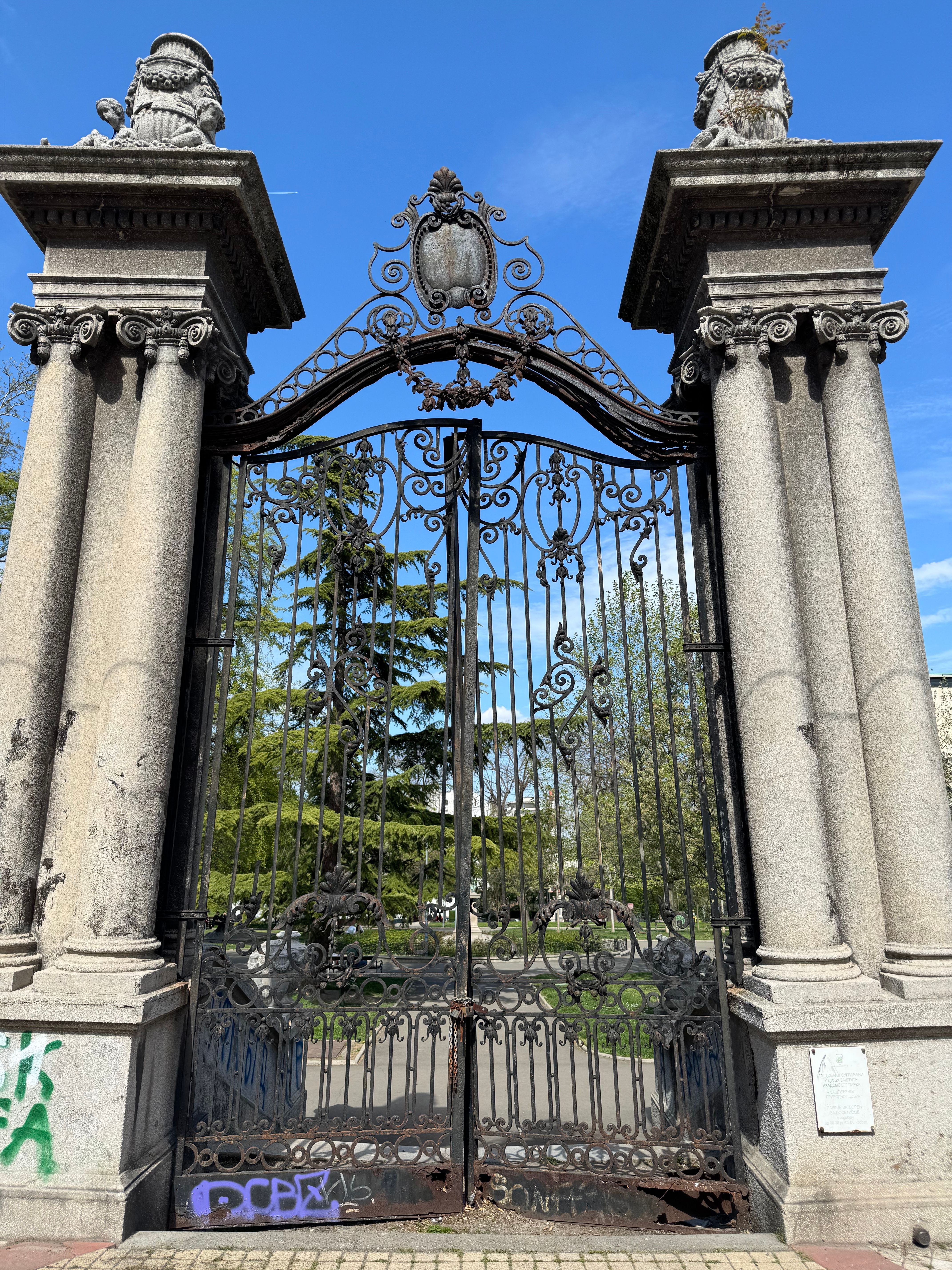 Historic wrought iron gate with stone pillars in Kalemegdan Park, Belgrade, under blue skies.