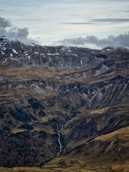 A breathtaking view of snowy mountain peaks with a cascading river and cloudy skies.