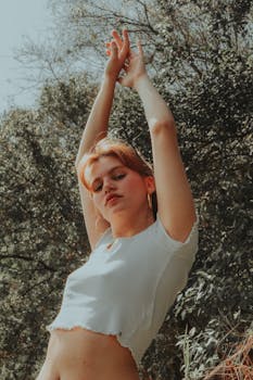 一名身穿白色上衣的红发女子在户外举起双臂摆姿势