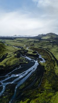 Stunning aerial capture of a meandering river through lush greenery and volcanic plains in Iceland.