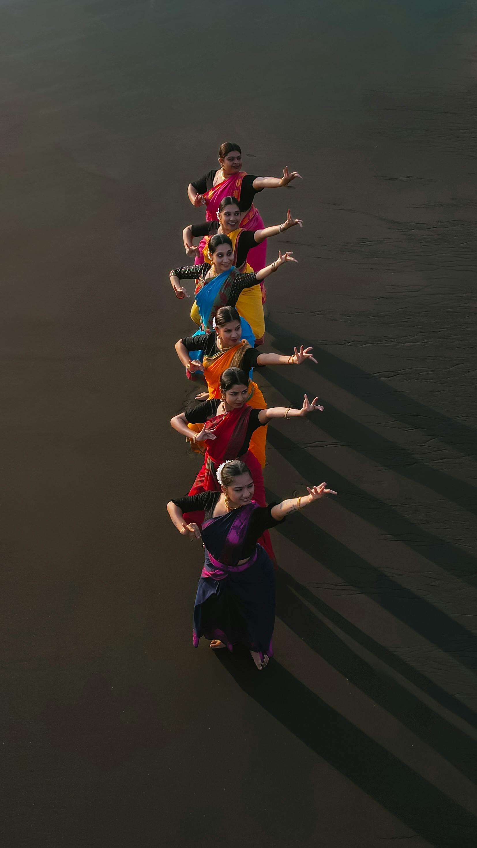 Group of women in colorful sarees performing traditional dance on a Mumbai beach.