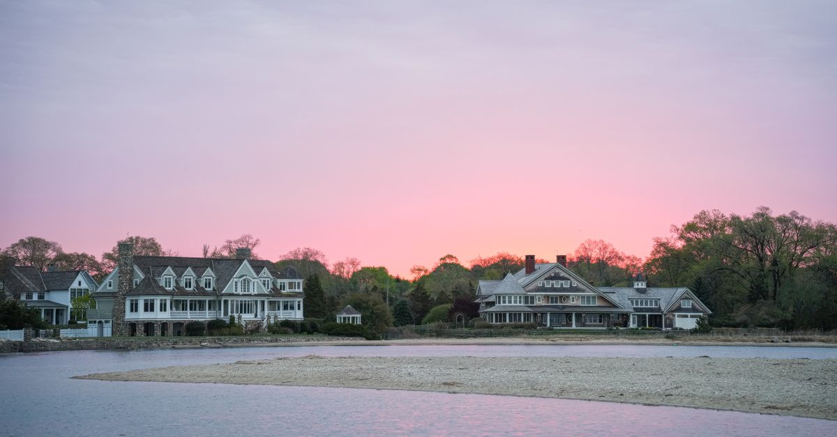 Charming waterfront homes at sunset with a vibrant pink sky over calm waters.
