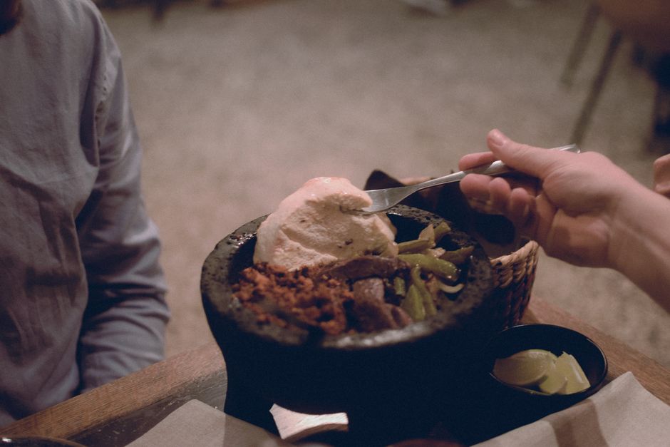 A rustic bowl of bright red-orange chile de árbol salsa with visible chile flecks, surrounded by toasted dried chiles and lime wedges on a wooden board.