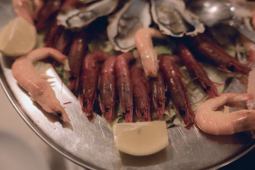 A delectable seafood platter featuring prawns, oysters, and lemons on a stainless steel plate.
