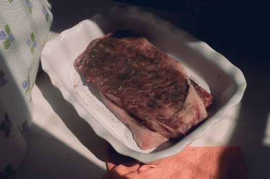 Marbled raw beef steak seasoned and ready in a baking dish, capturing natural light.