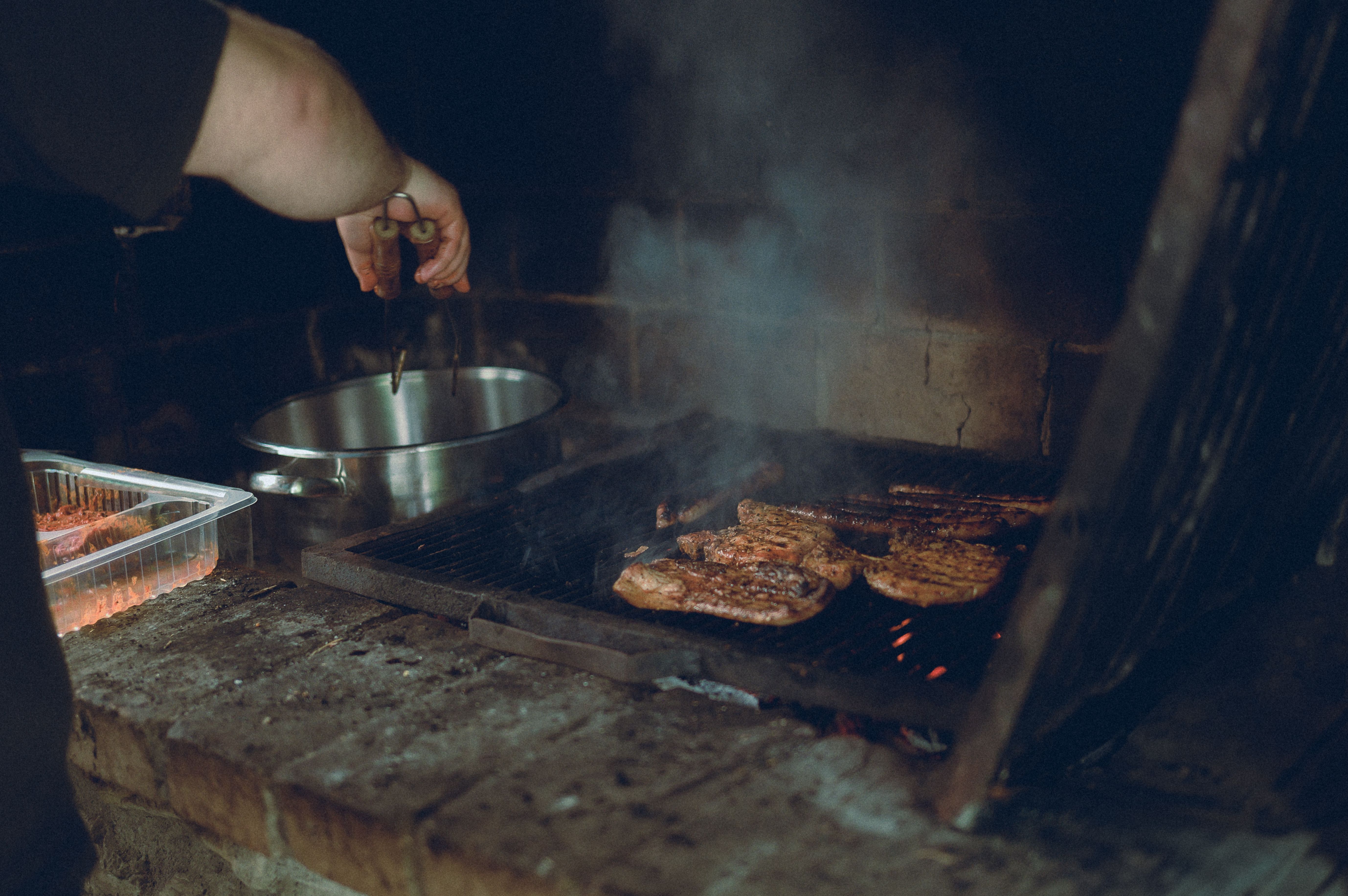 Main du grillardin à la pince au-dessus des pièces de viande sur la braise, foyer en briques