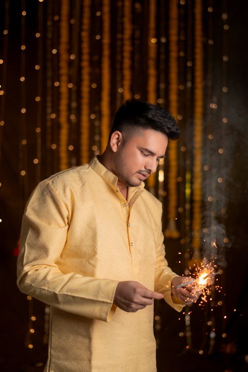 Free A man in traditional attire lights sparklers indoors for Diwali celebration. Stock Photo