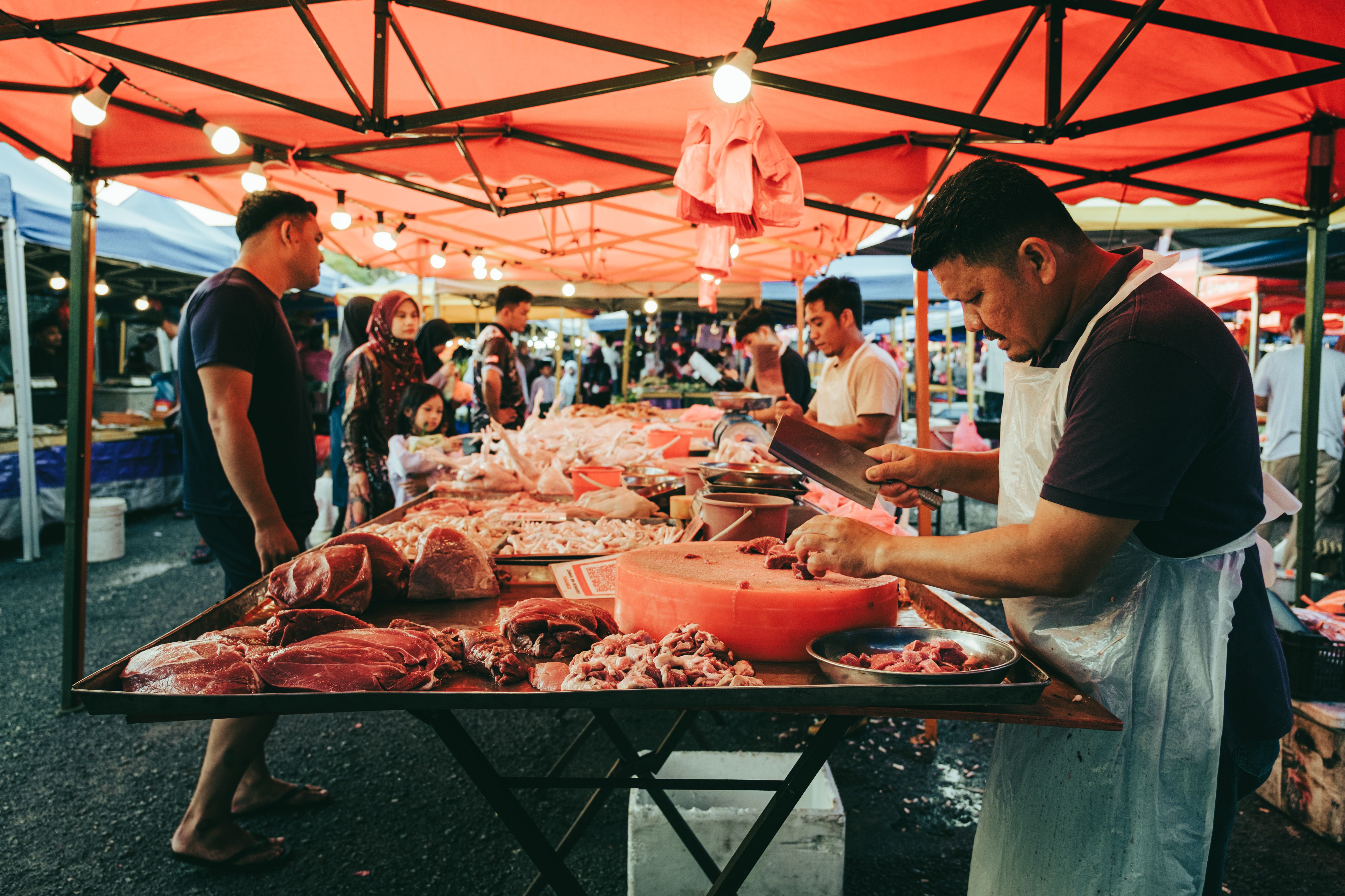 gratis Een slager snijdt vlees op een drukke avondmarkt in Sepang, Maleisië, en laat zo de lokale cultuur zien. Stockfoto