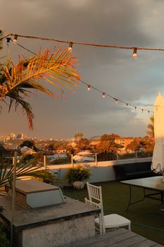 A rooftop view at sunset with Sydney's skyline. Features string lights and palm trees for a serene atmosphere.
