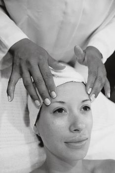 A close-up black and white photograph of a woman receiving a relaxing facial treatment in a spa setting.