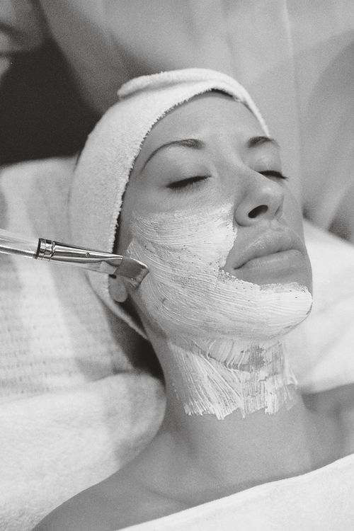 Free Black and white image of a woman receiving a facial mask treatment at a spa. Stock Photo