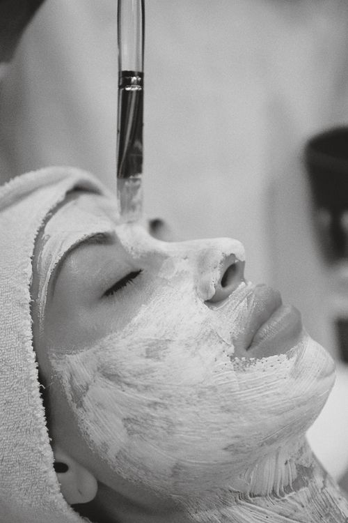Free Black and white close-up of a woman receiving a facial mask treatment at a spa. Stock Photo