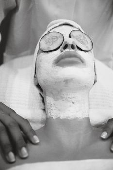 A person enjoying a soothing spa facial with a white mask and cucumber slices over eyes.