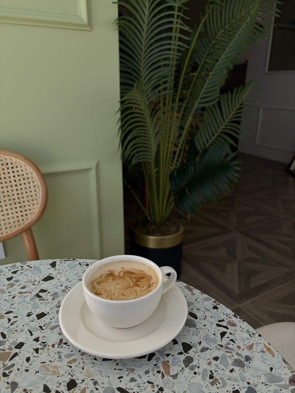 A serene cafe scene featuring a steaming cup of coffee on a terrazzo table with green decor.