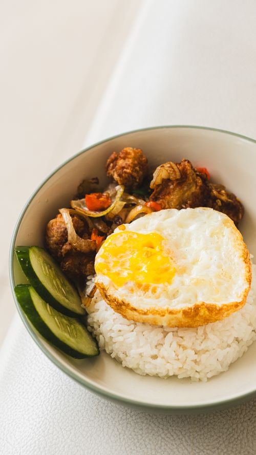 Free Bowl of rice with fried egg, chicken, and cucumber slices, perfect for an Asian cuisine feature. Stock Photo