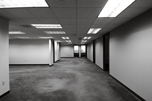Black and white image of an empty office space with fluorescent lighting and exit sign.