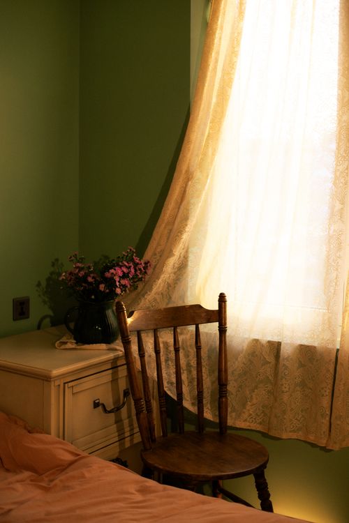 Free Warm and cozy bedroom corner with wooden chair, floral arrangement, and lace curtains. Stock Photo