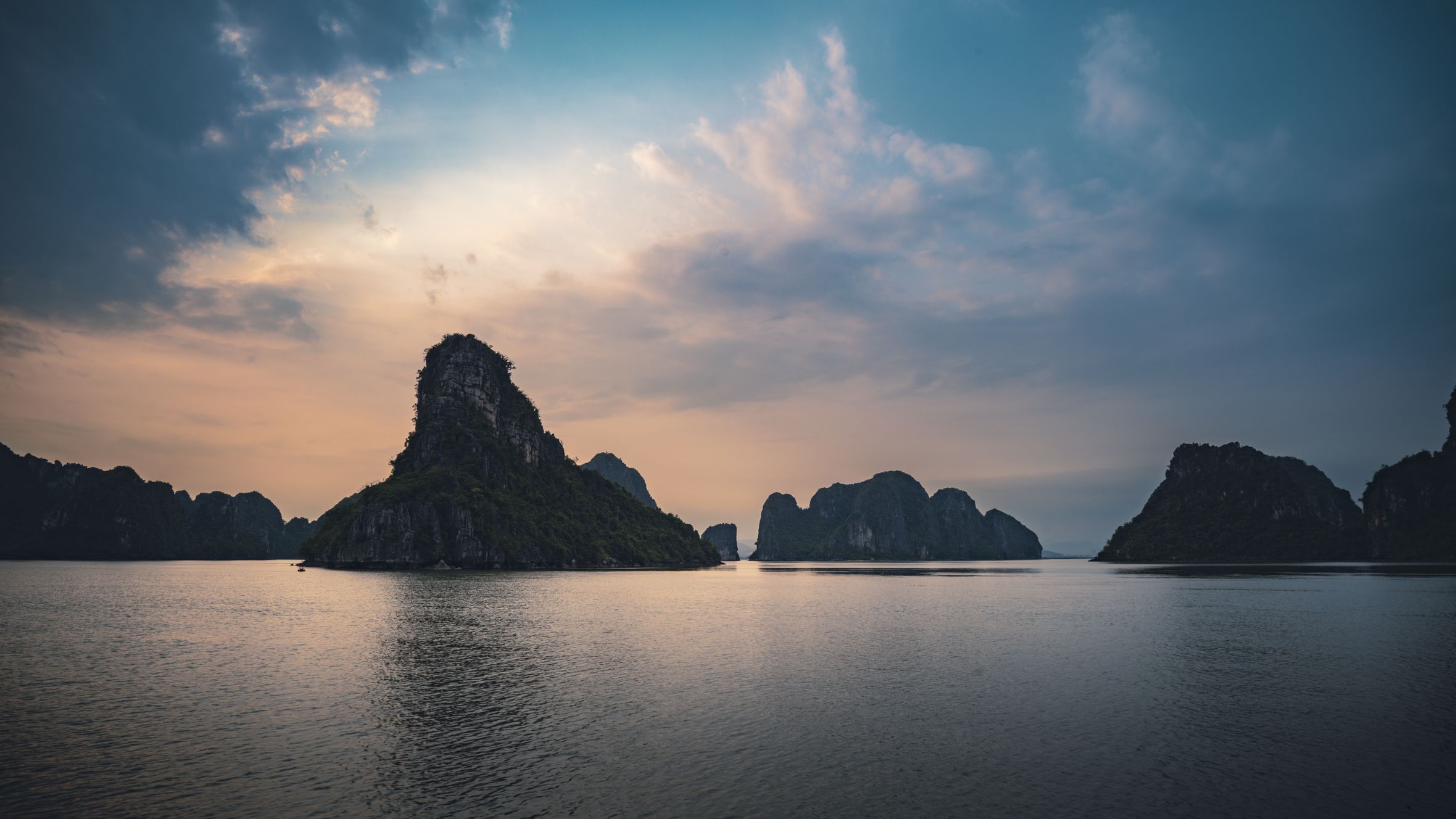 Stunning sunset over Halong Bay, Vietnam, with karst formations reflected in the tranquil waters.