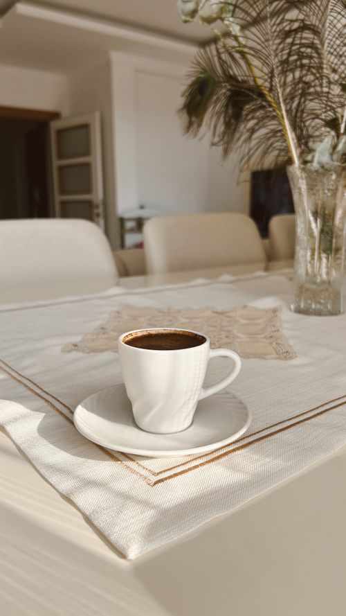 Free A classic white coffee cup sits elegantly on a sunlit dining table with a decorative vase. Stock Photo
