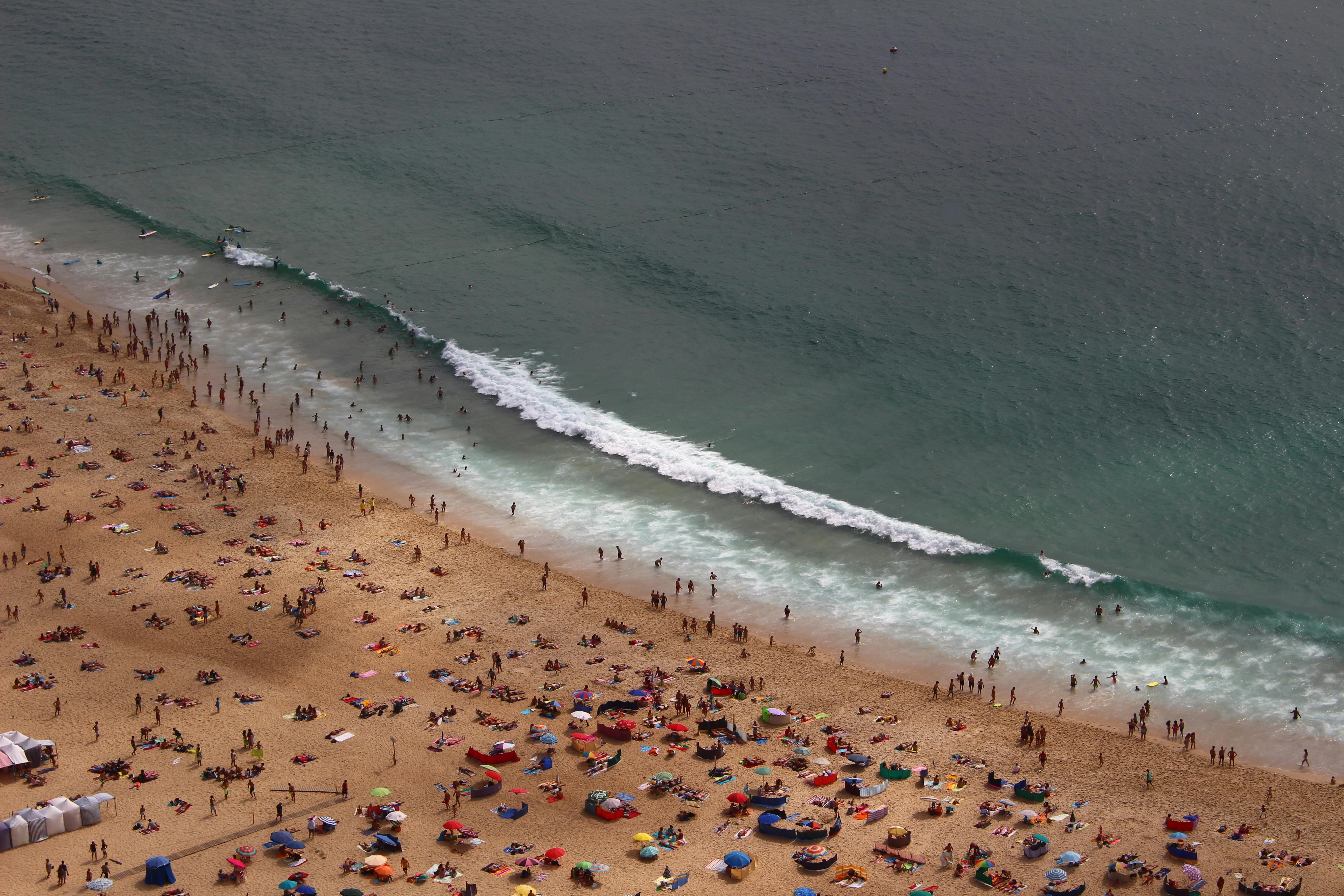 Aerial view of a busy sandy beach with sunbathers and swimmers along the shoreline as waves roll in