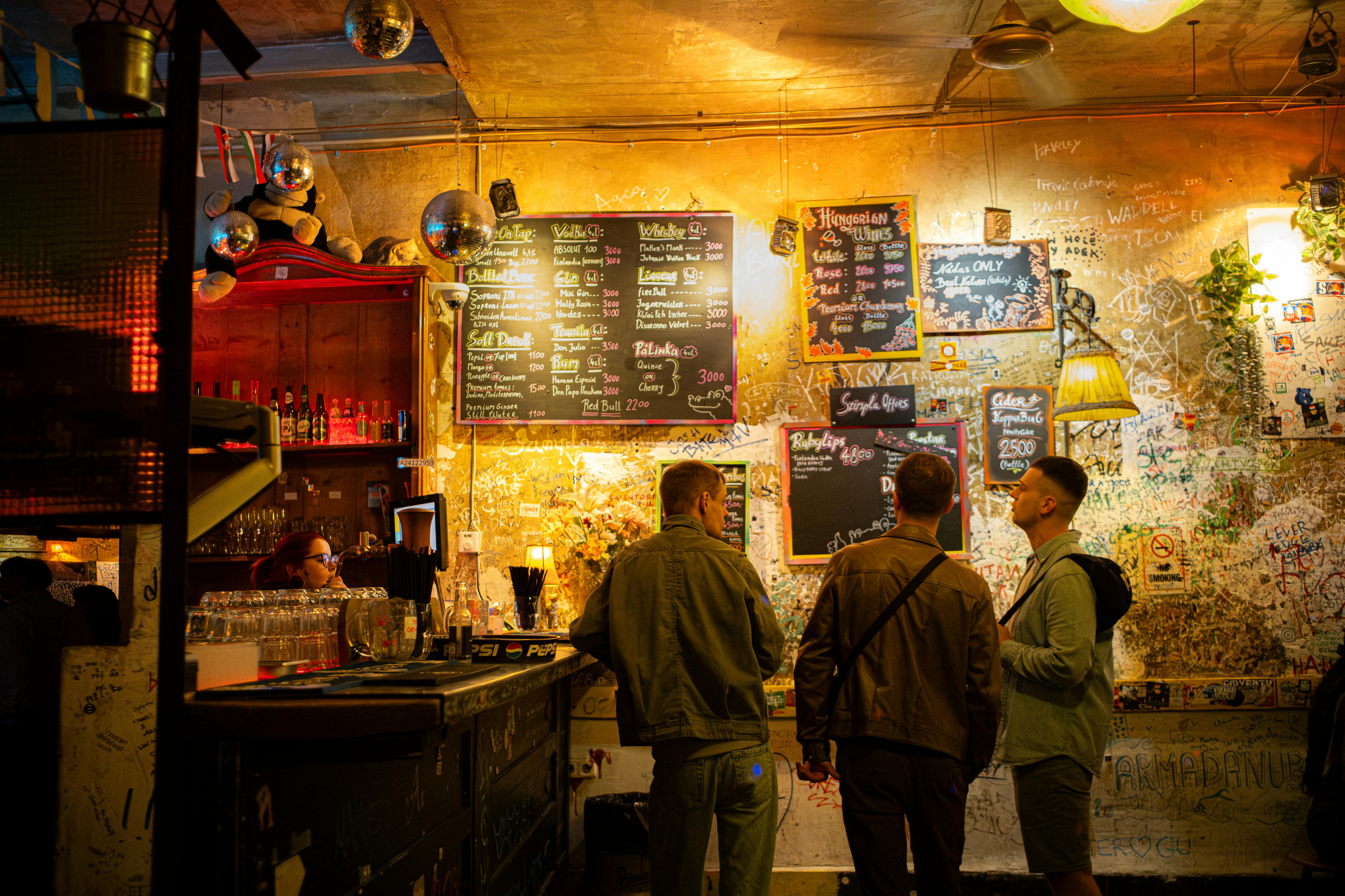 鮮やかな照明のもと飲み物を語らうブダペストのルインパブの3人 — Szimpla Kert 定番のルインバーの雰囲気