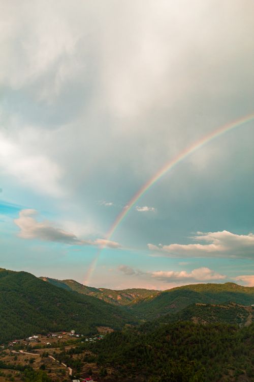 Free Beautiful view of a rainbow spanning over verdant hills and a cloudy sky. Stock Photo