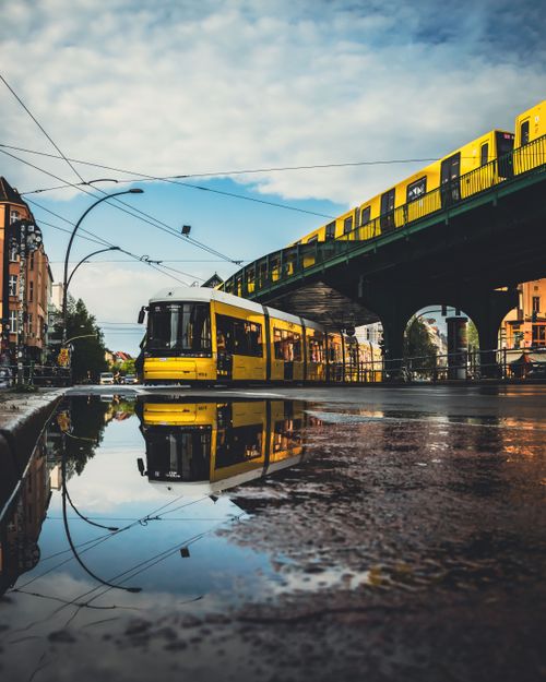 Free Yellow tram and elevated train in Berlin, Germany, reflected in street puddle. Stock Photo