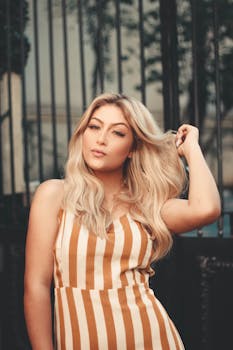一位优雅的金发女性身着条纹连衣裙，在户外自信地摆出姿势，展现着时尚与美丽