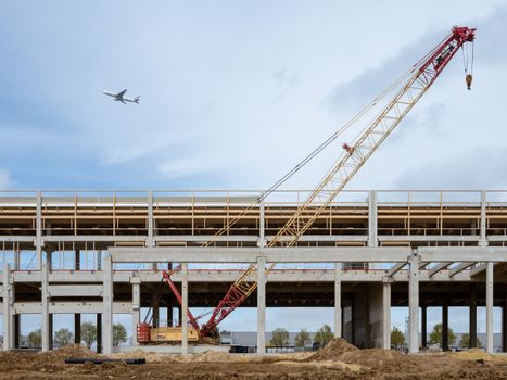 A large crane at a construction site with a plane flying overhead, set against a clear sky.