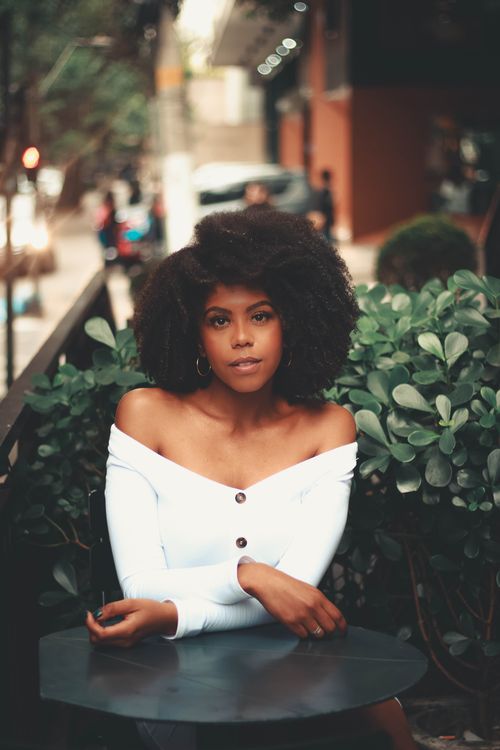 Free Beautiful woman with afro hairstyle sitting outdoors in urban setting, showcasing elegance and style. Stock Photo